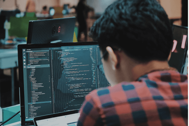 A person sitting at a computer screen with development code on screen.