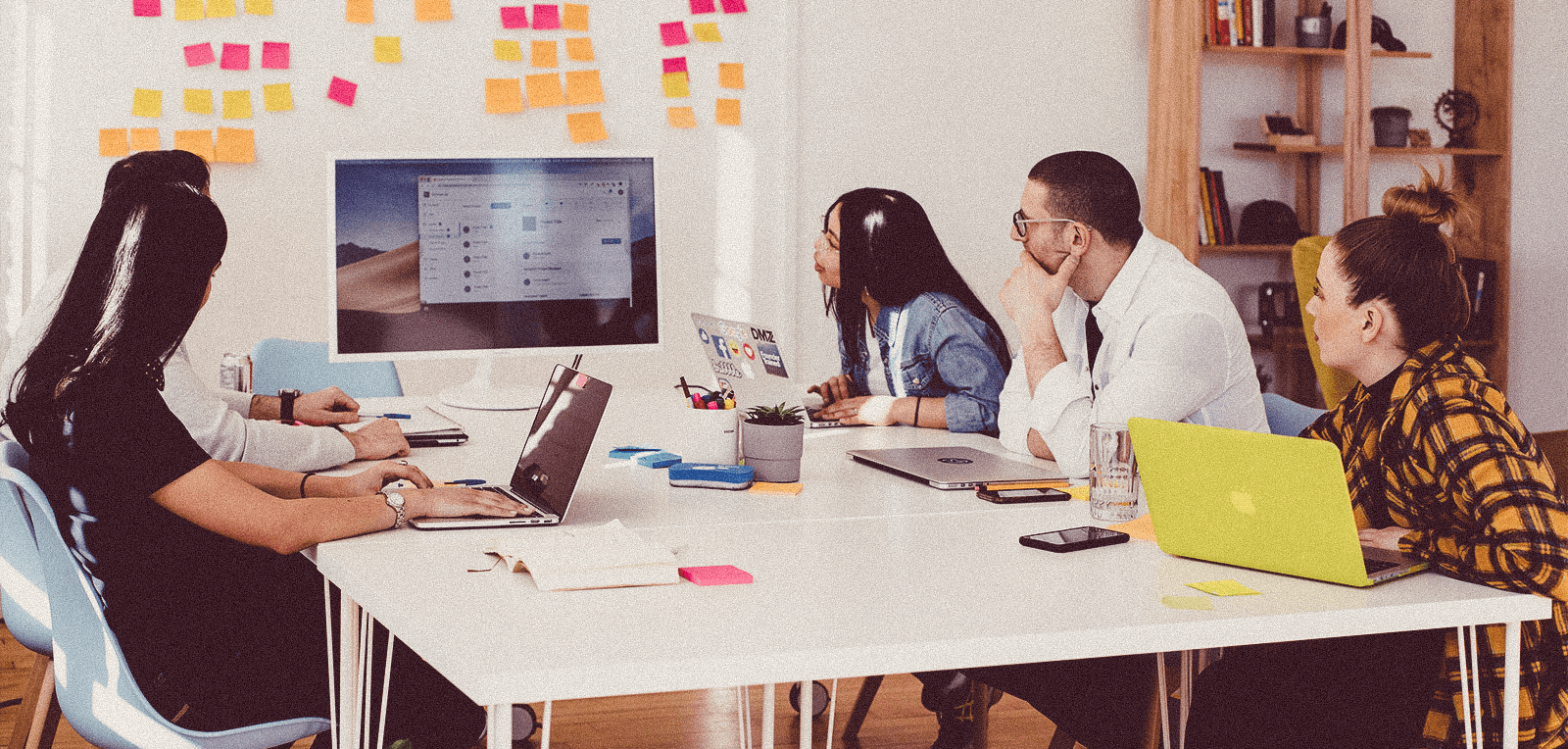 Four coworkers in a meeting looking at a whiteboard full of ideas on post-its