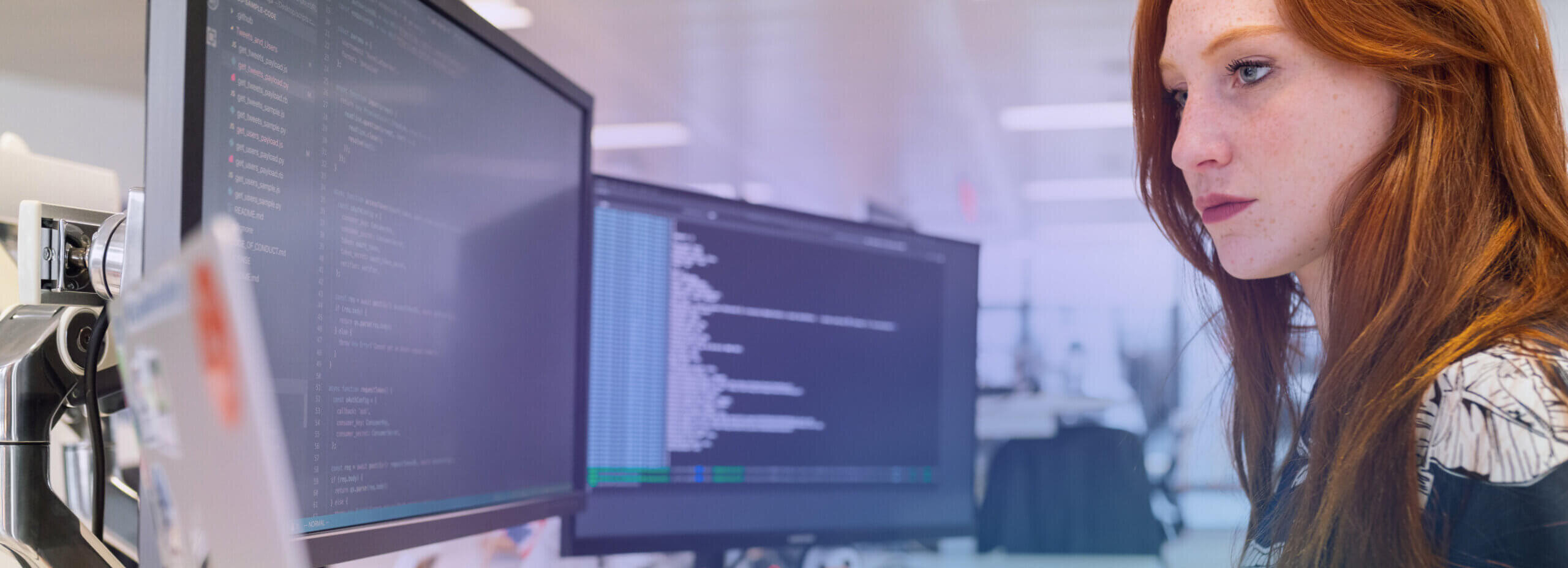 Woman coding at her desk looking at two monitors