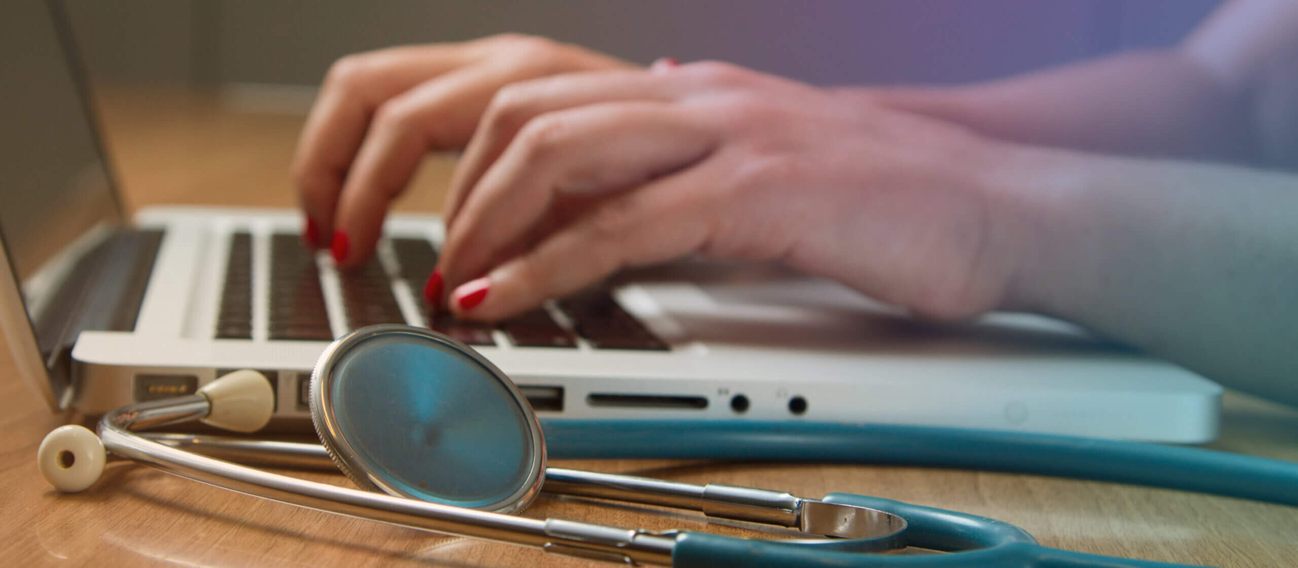 Person on a laptop next to a stethoscope