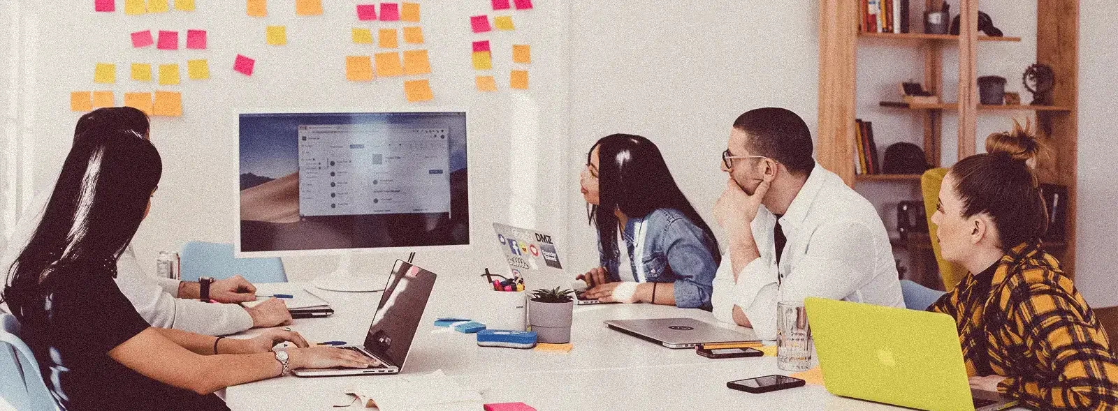 Four coworkers in a meeting looking at a whiteboard full of ideas on post-its