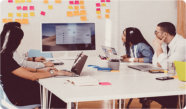 Four coworkers in a meeting looking at a whiteboard full of ideas on post-its