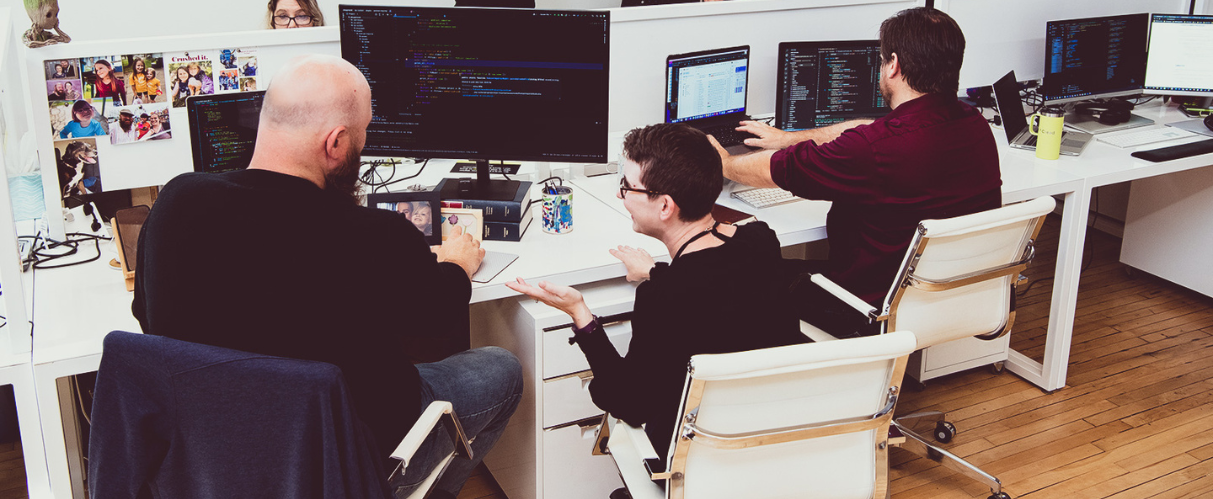Creed employees talking while sitting at their desks with computers